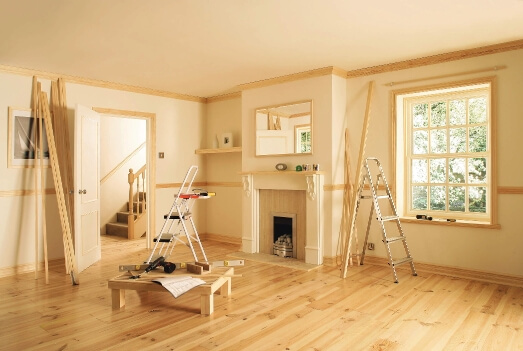 A modern living room with wooden floors; a DIY project is in progress with ladders and various raw materials scattered around